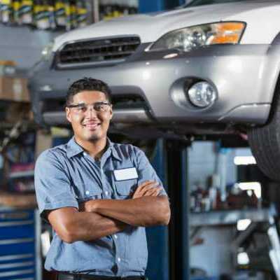 auto service technician standing in front of car on a lift with a toolbox behind it