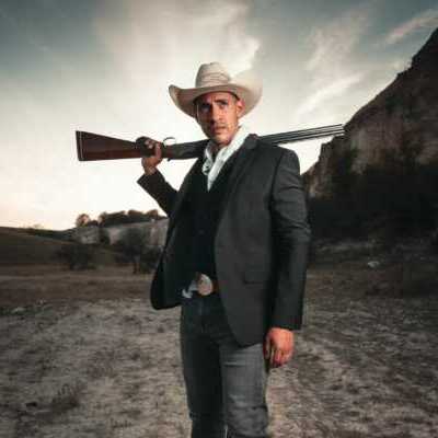 man dressed like cowboy with shotgun on his shoulder